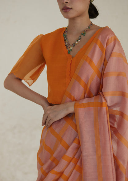 Handloom silk modal saree from Surmaye, having a check pattern with shades of pink and orange. Paired with orange designer blouse, with scalloped embroidery edges all over.