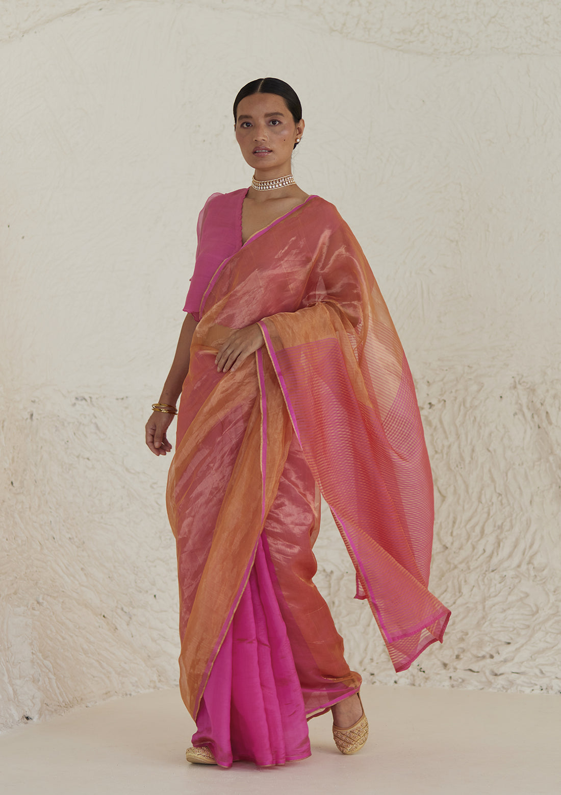 Handloom silk saree in dual colour, from Surmaye. Pink organza mulberry silk panel till pleats, followed by orange silk zari panel and pink stripes at the pallu edge.